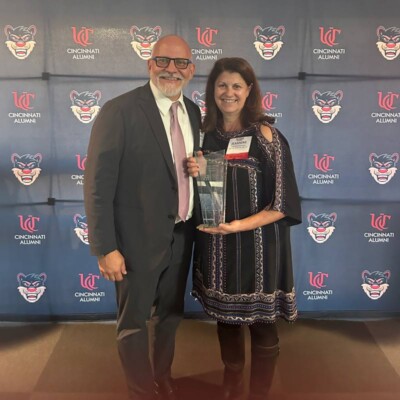 Woman holding an award next to a man in front of University of Cincinnati step and repeat banner